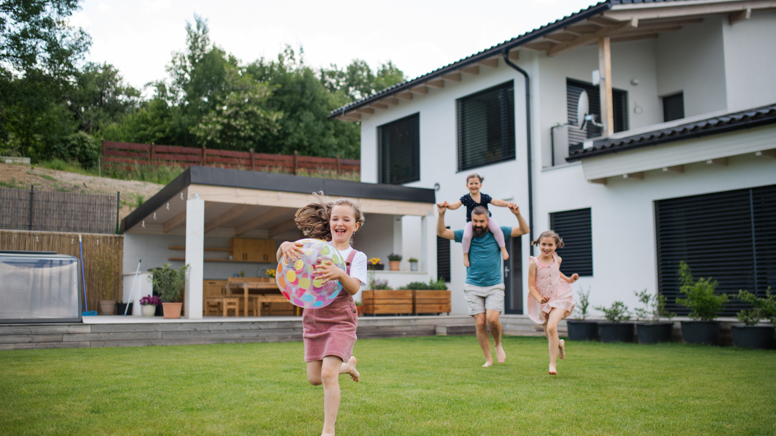 Father and daughters running playfully in backyard.